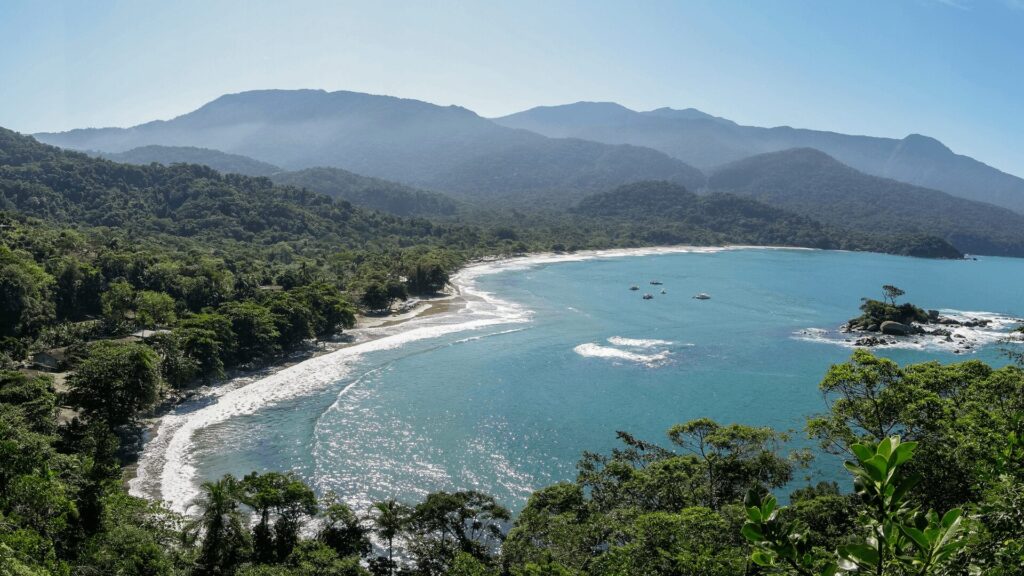 Vista panorâmica da praia e montanhas com árvores verdes exuberantes em primeiro plano.
