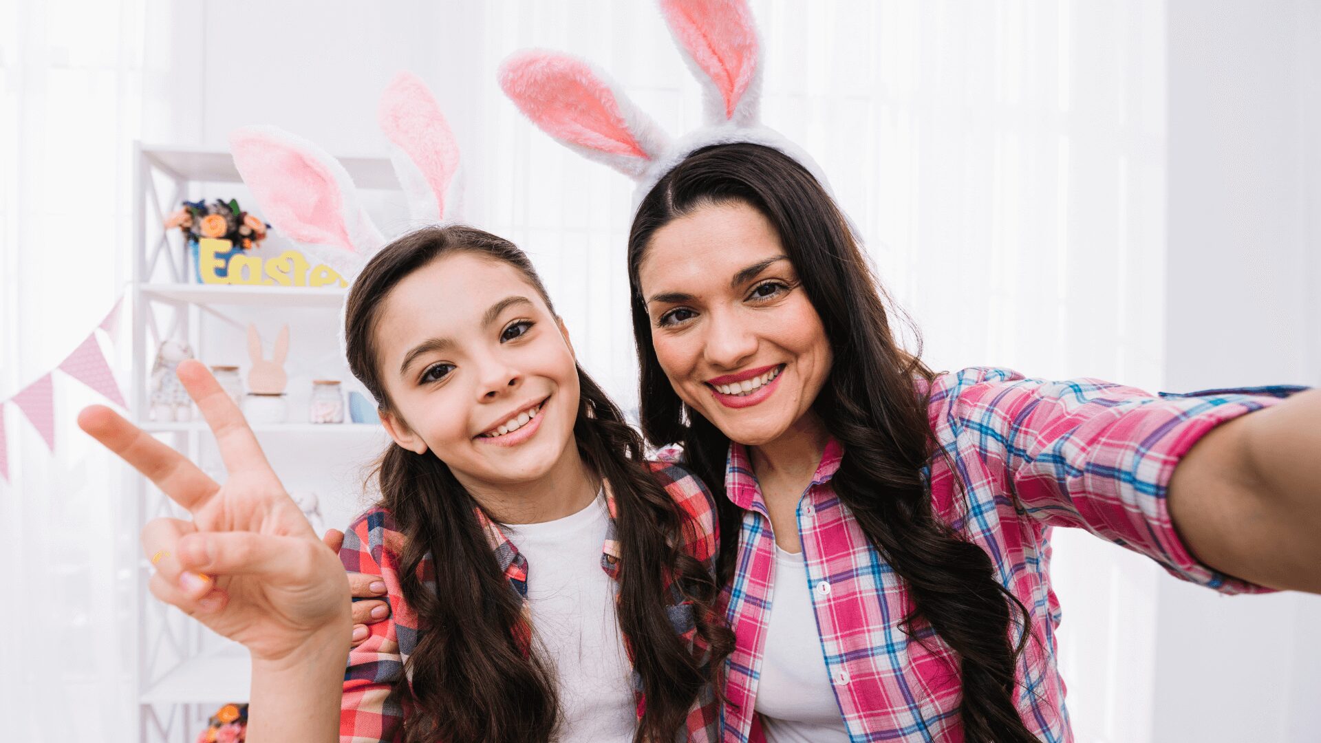Uma selfie de duas garotas usando tiaras de coelhinho, fazendo o "V" da paz, com um cenário festivo de Páscoa.