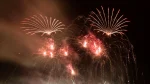Dois grandes conjuntos de fogos de artifício em forma de leque ou palma, com raios vermelhos-alaranjados brilhantes se estendendo para fora, um à esquerda e outro à direita. Eles parecem ser as explosões principais.