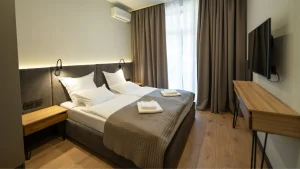 Quarto de hotel moderno e aconchegante com duas camas de solteiro juntas, móveis de madeira clara e iluminação suave embutida na cabeceira.