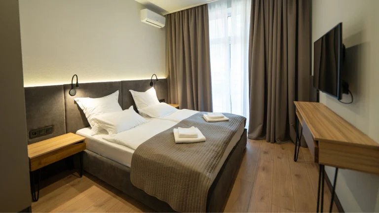 Quarto de hotel moderno e aconchegante com duas camas de solteiro juntas, móveis de madeira clara e iluminação suave embutida na cabeceira.