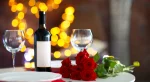 Mesa posta para jantar romântico com garrafa de vinho tinto, duas taças de cristal e buquê de rosas vermelhas, com luzes desfocadas ao fundo.
