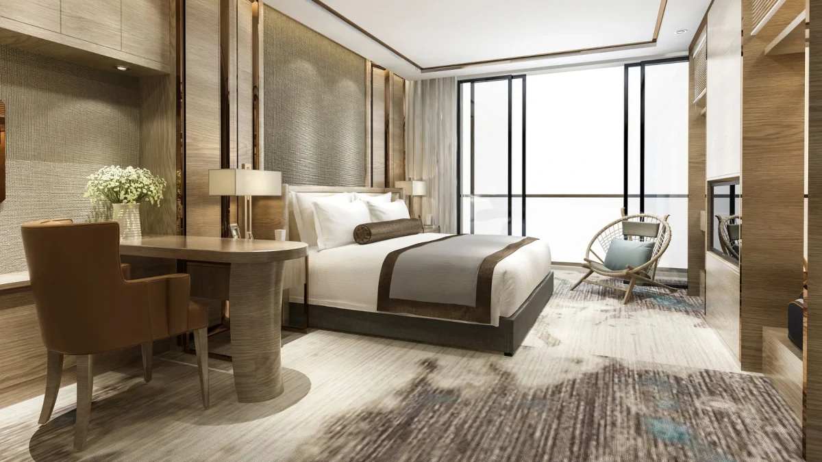 Quarto de hotel estilo lifestyle moderno e elegante, com cama de casal arrumada em tons neutros, bancada de trabalho em madeira com cadeira de couro, poltrona de vime no canto e grandes janelas com iluminação natural.