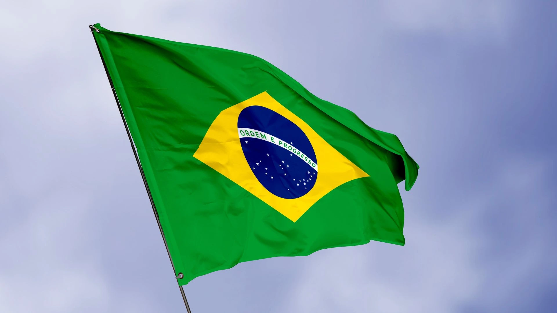 Bandeira do Brasil hasteada e balançando em um mastro em um céu nublado, simbolizando a celebração do feriado de 7 de setembro.