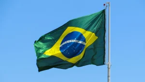 Bandeira do Brasil tremula ao vento em um mastro, sob céu azul e claro. O símbolo verde, amarelo e azul representa o país.